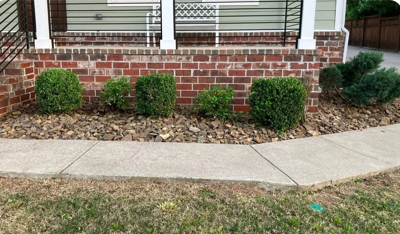 Front bed along a brick porch after a cleanup: shrubs pruned, weeds cleared and the edge cleaned up