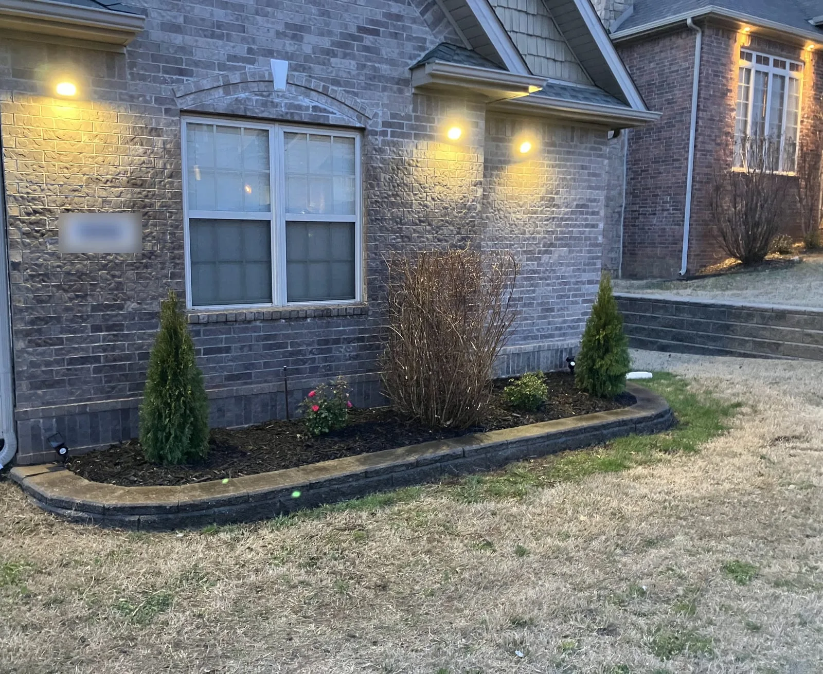 Brick home at dusk with lights on the wall above a curbed front bed
