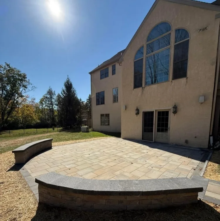 Paver patio with a curved stone seat wall behind a tall stucco home