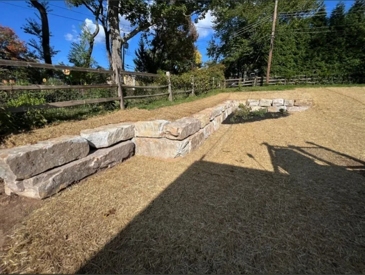 Low border of large cut-stone blocks outlining a raised area in a newly graded, strawed yard
