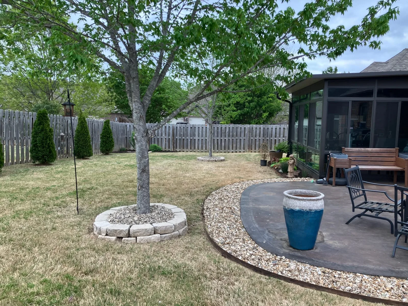 Backyard with a stone ring around a young tree and a gravel border edging a stamped patio