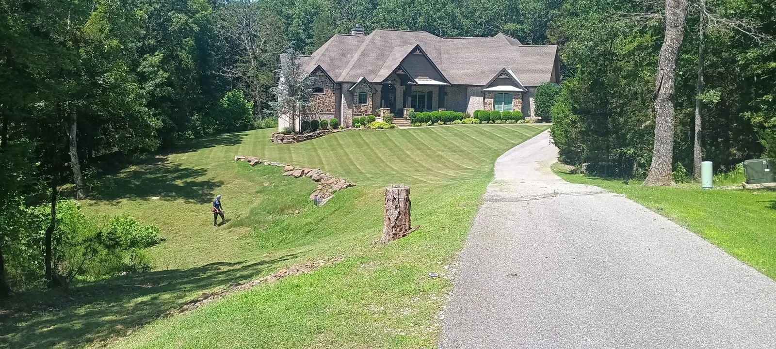 Freshly striped lawn sloping up to a brick home beside a long driveway